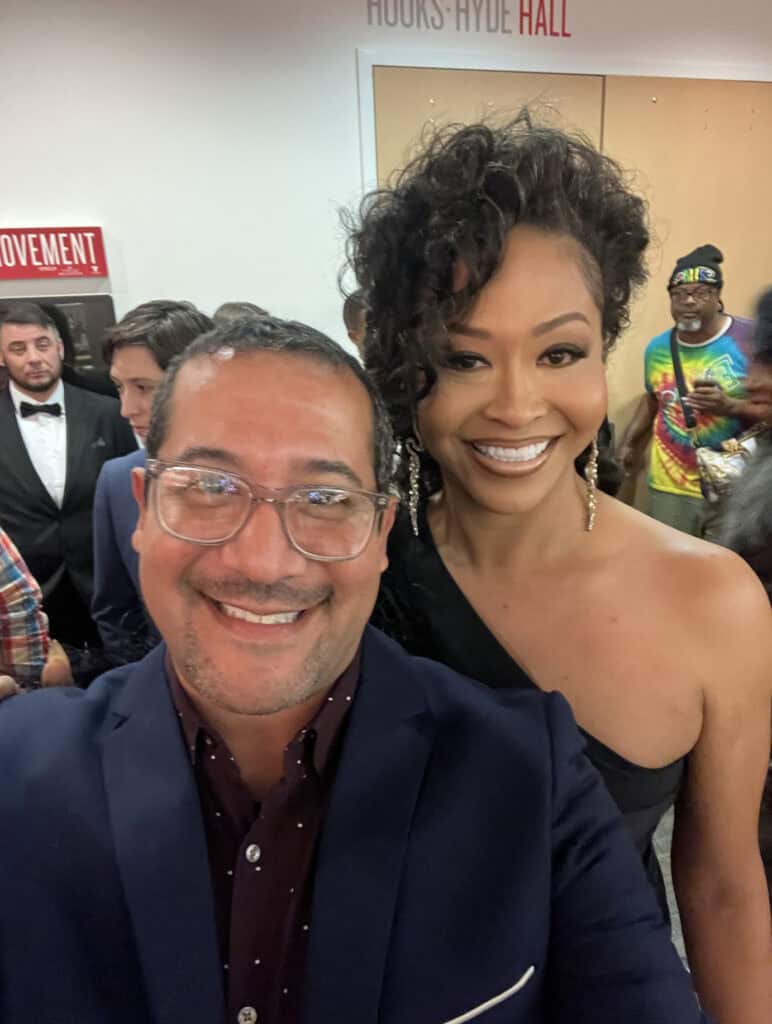 Ray Rico and Jasmine Tasaki in a selfie in front of several other people in a bright room.